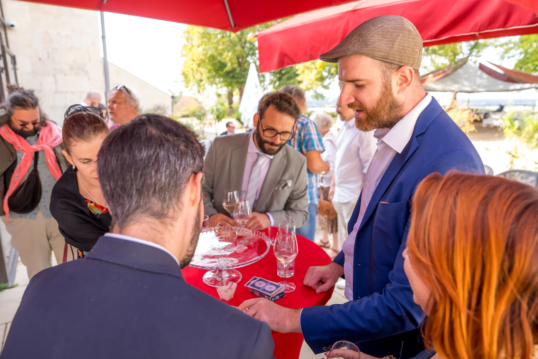 Ugo avec un H joue un tour de cartes au vin d'honneur, autour d'une table haute nappée de rouge