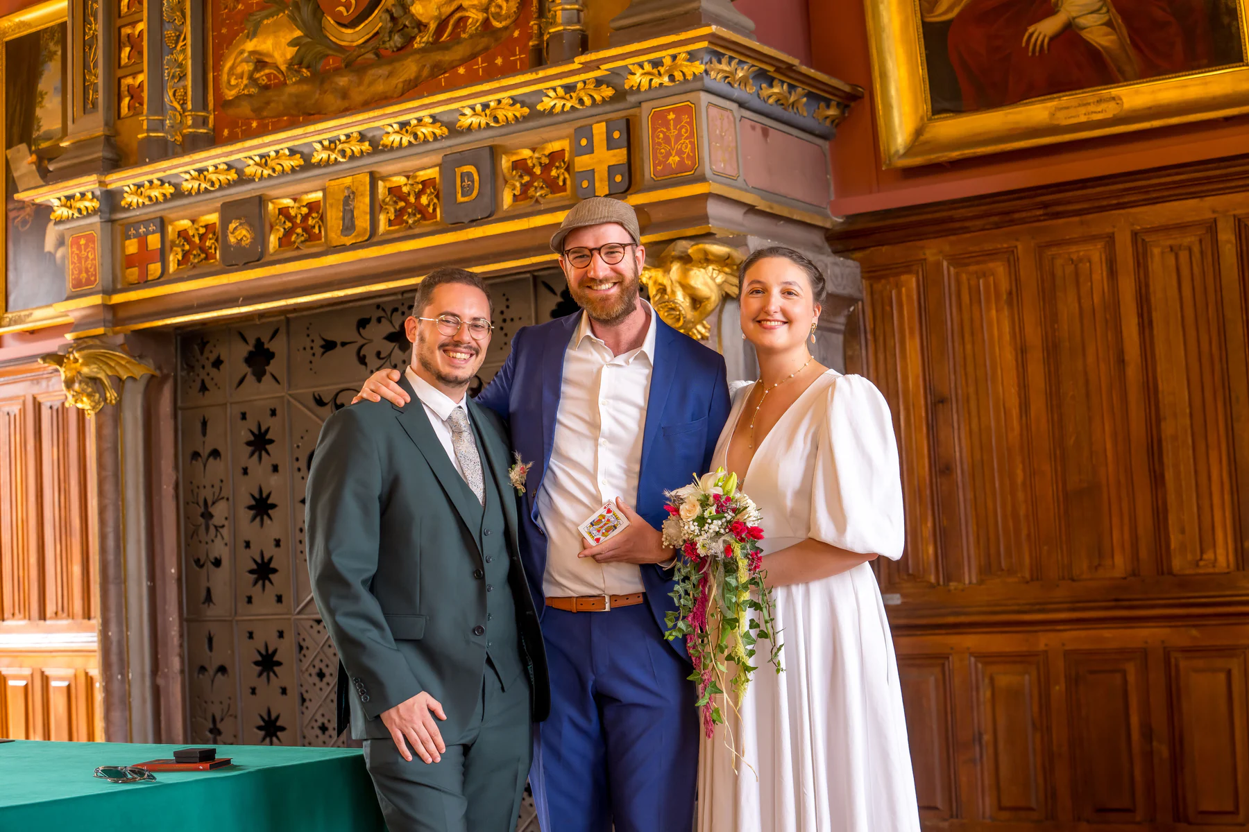 Ugo avec un H pose entre les mariés dans une salle aux boiseries dorées